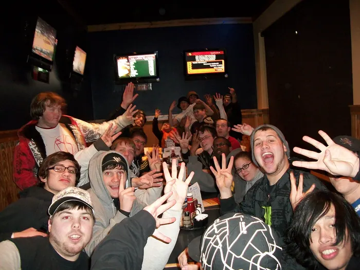 Crew packed together indoors at night after a show, hands up for the camera
