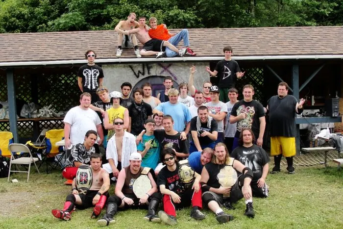 Crew photo in front of a pavilion, several wrestlers holding title belts