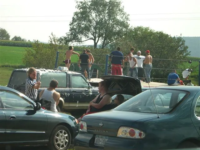 A match running between parked cars with a referee and the crowd watching from the hoods